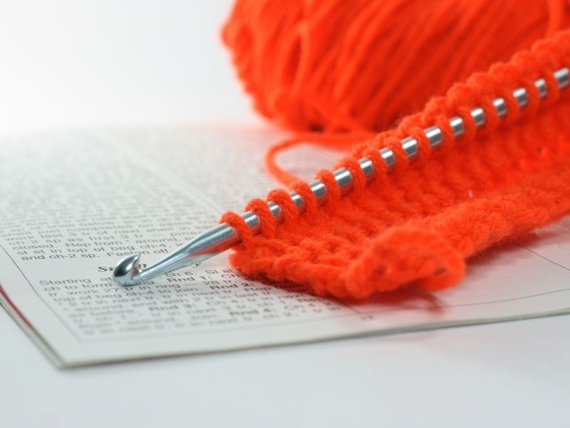 An orange crochet ball is sitting on top of an open book.