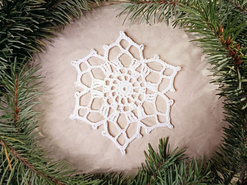 A white snowflake is placed in a wreath of pine branches.