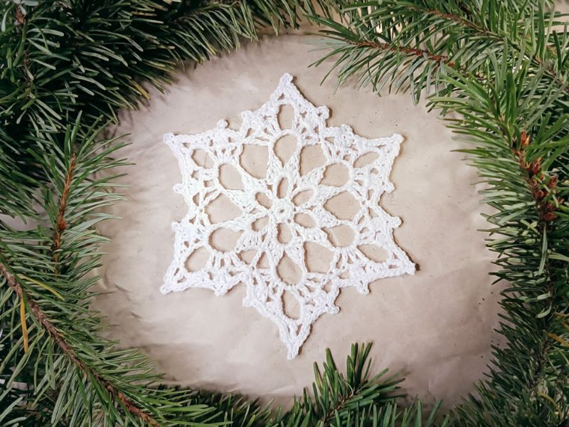 A white snowflake is surrounded by pine branches.