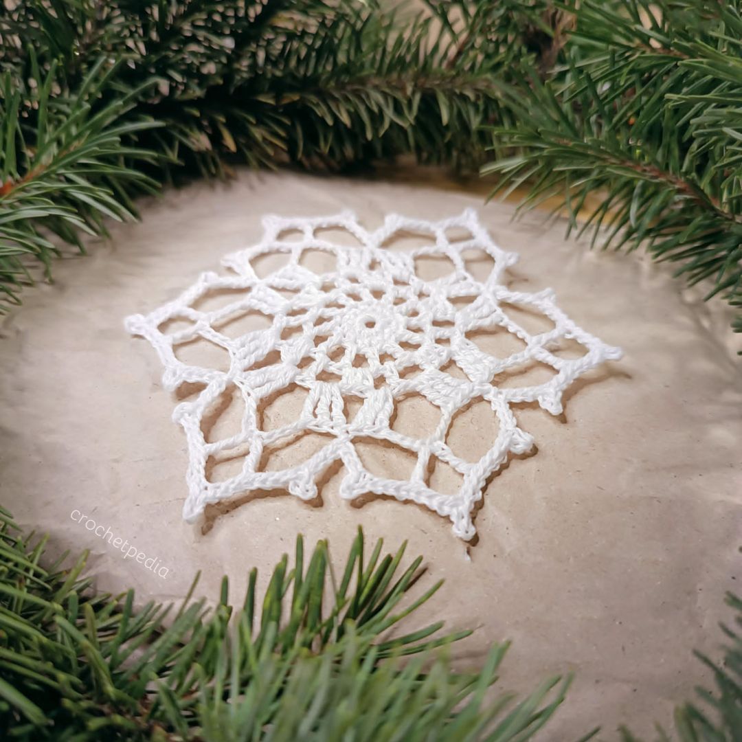 A small crocheted snowflake on top of a pine tree.