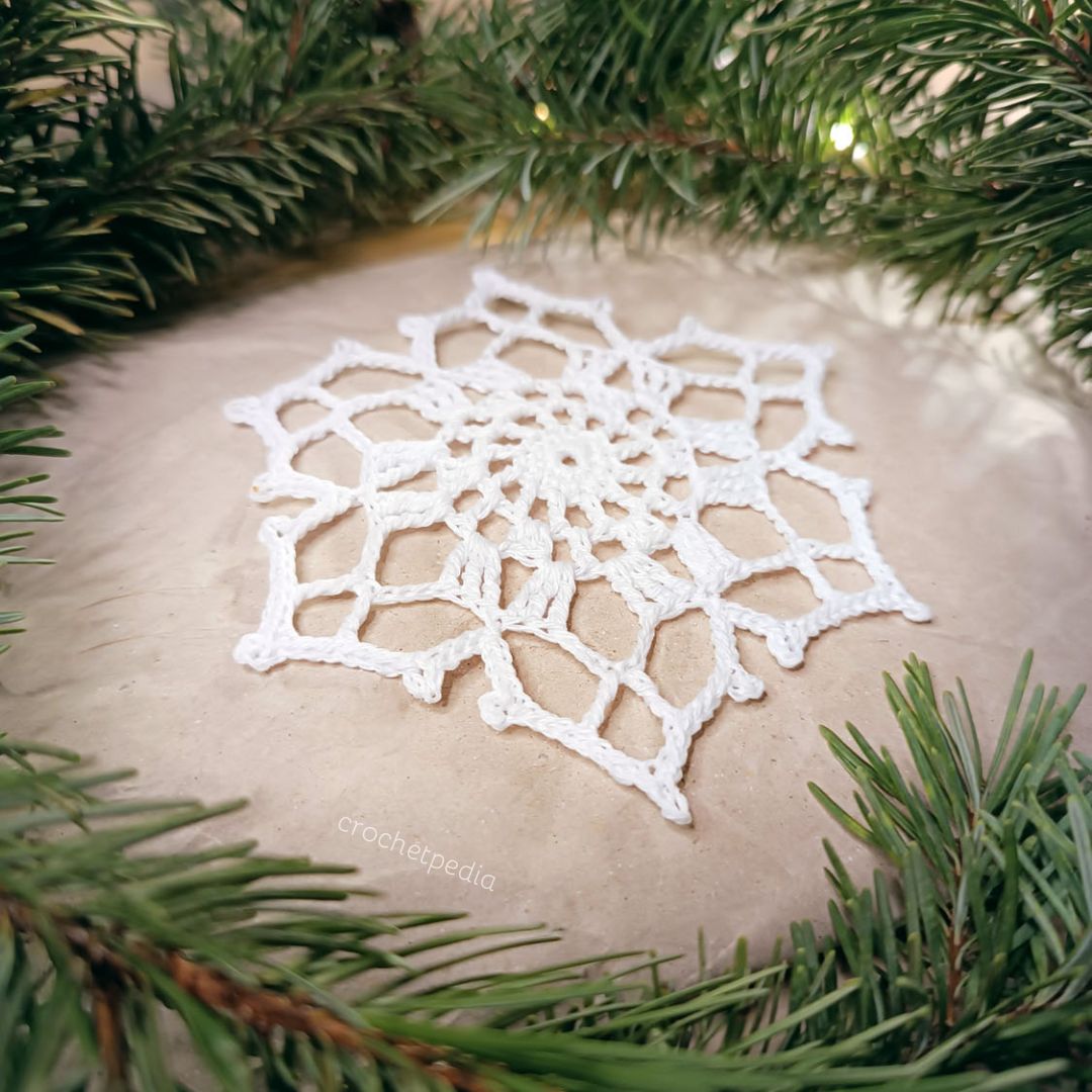 A white crocheted snowflake on top of a pine tree.