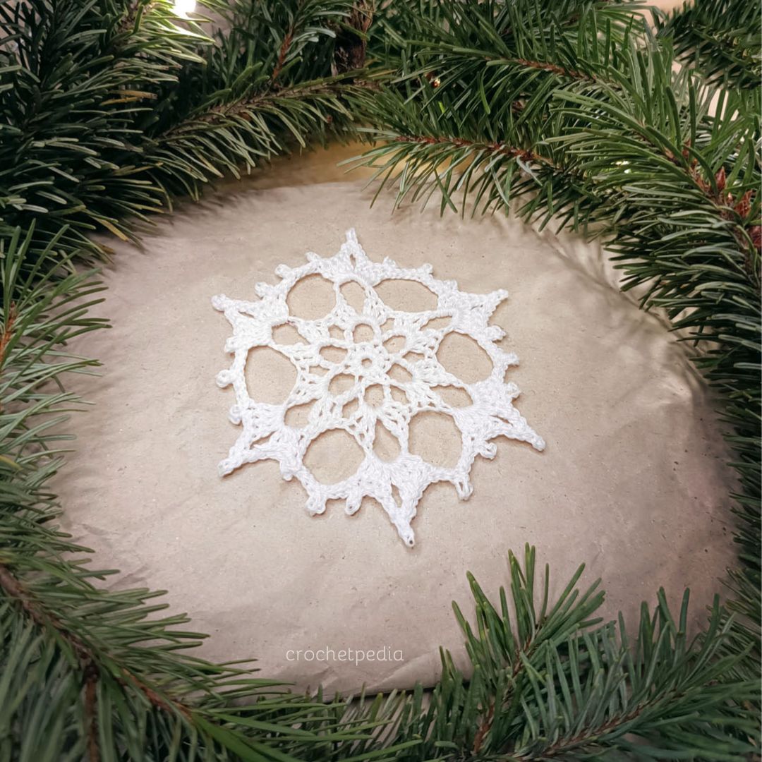 A white snowflake is sitting on top of a pine tree.