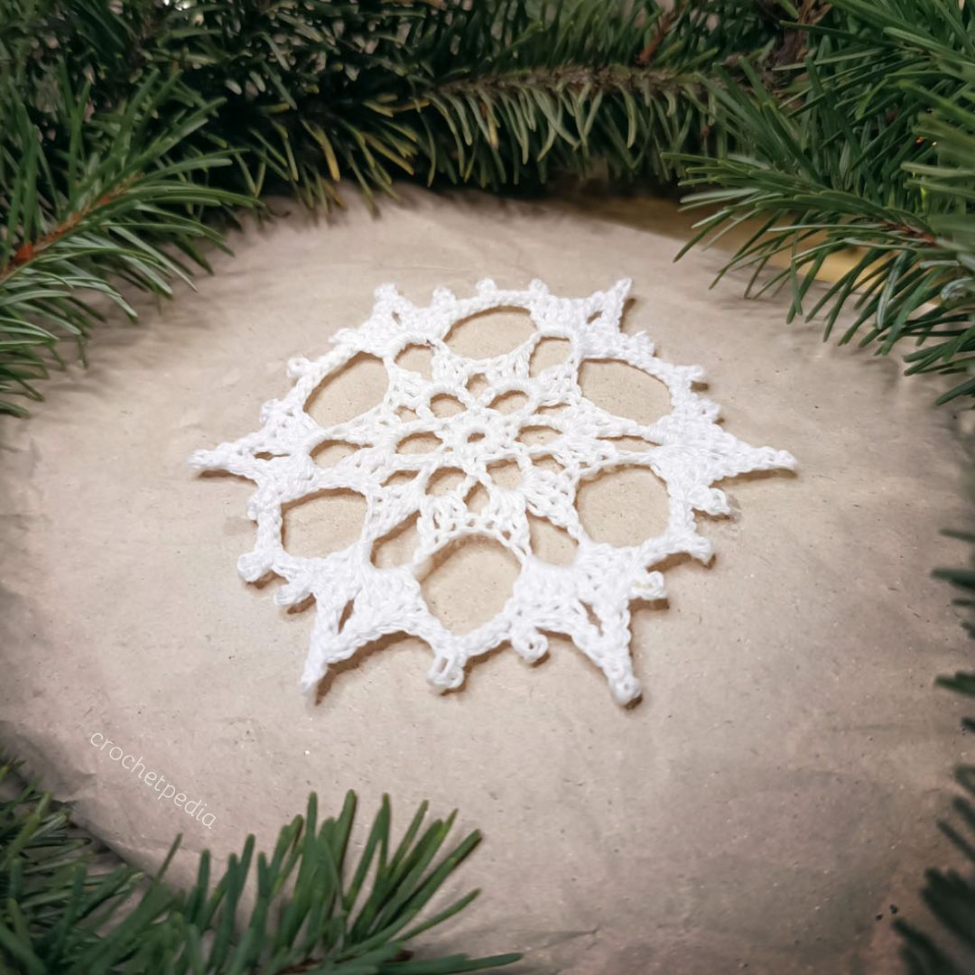 A white crocheted snowflake on top of a pine tree.