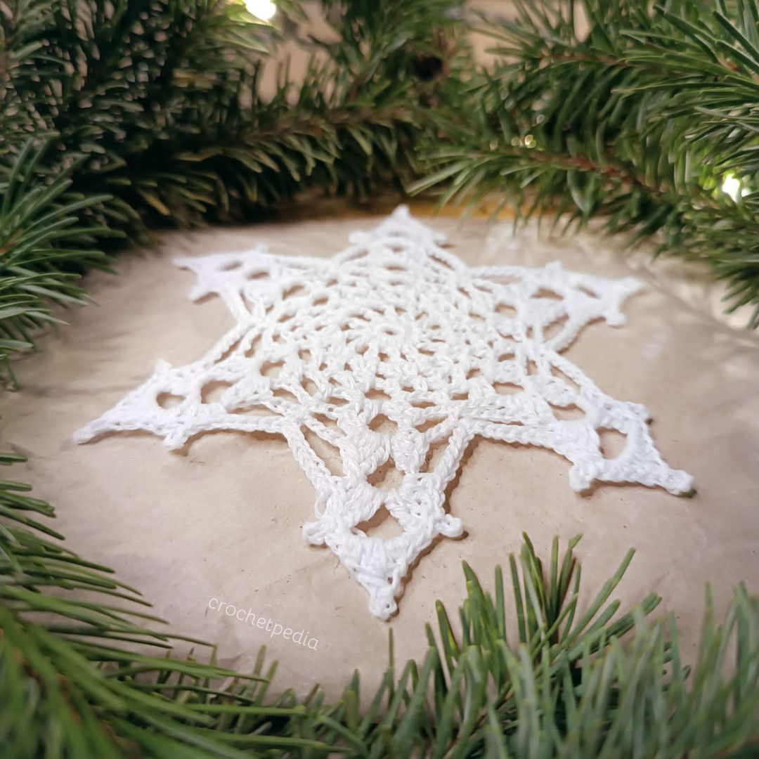 A white crocheted snowflake on top of a christmas tree.