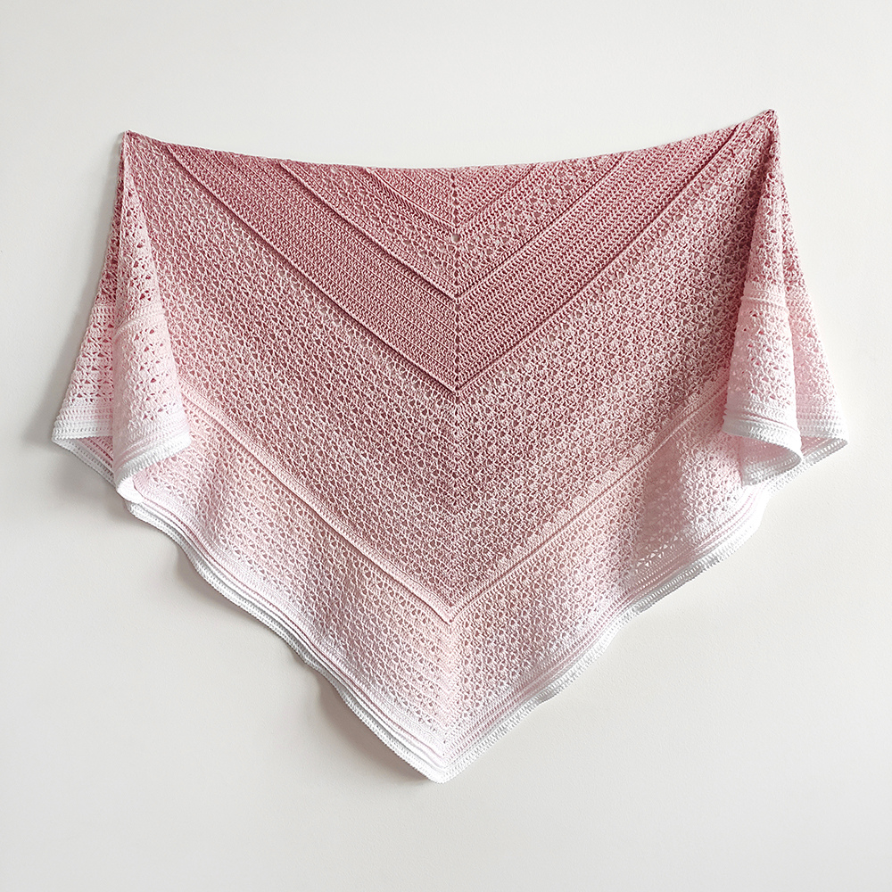Handcrafted magnolia pink gradient knitted shawl displayed on a white background.